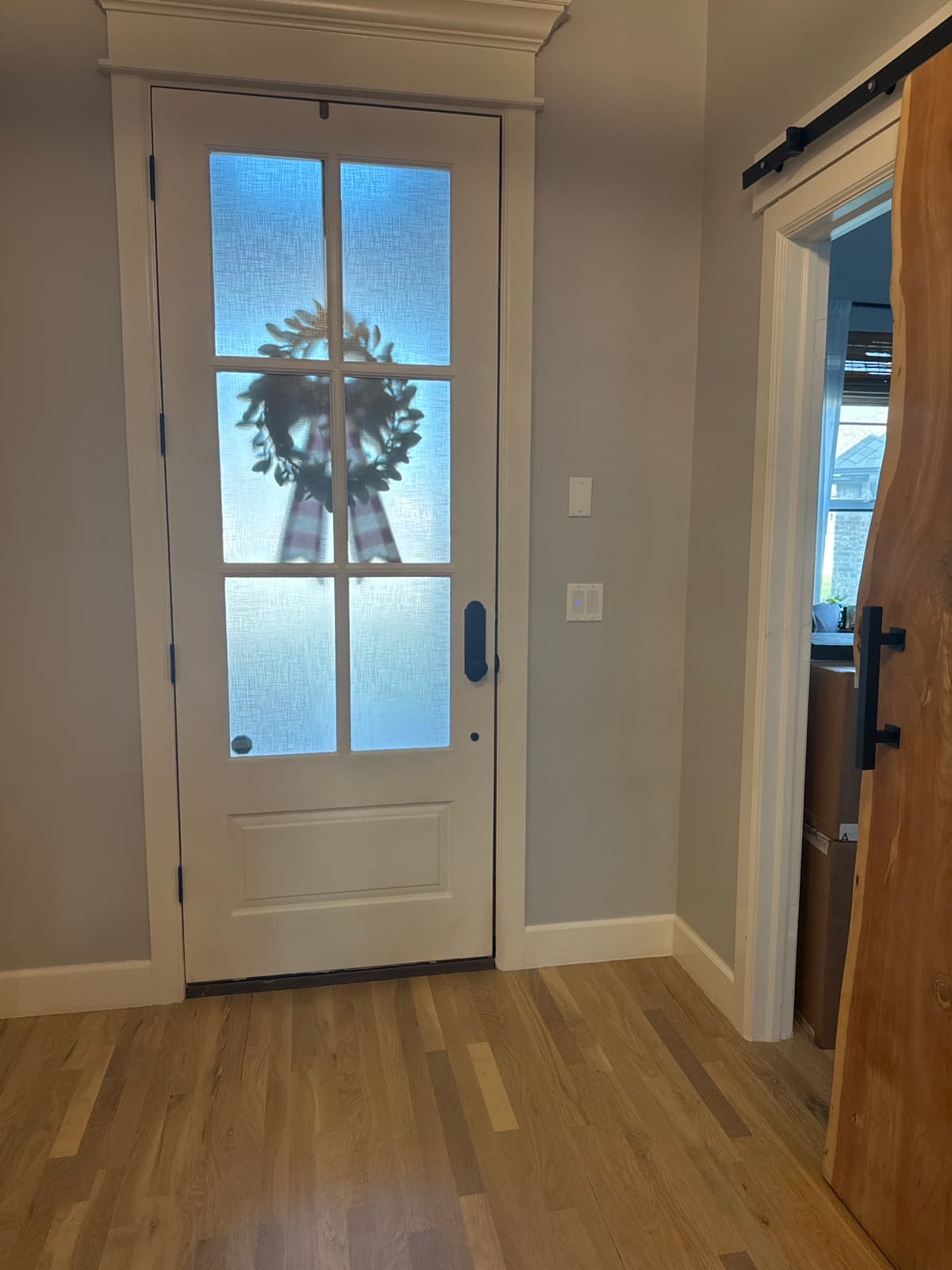 Adjusted white full-lite front door with a wreath, opening onto refinished hardwood floors